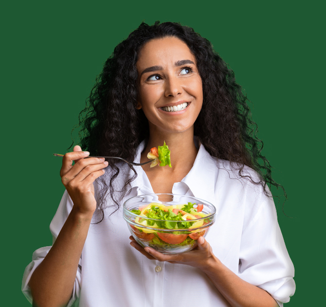 Photo of a young woman of Latin or Greek heritage smiling and enjoying a healthy green salad with tomatoes.