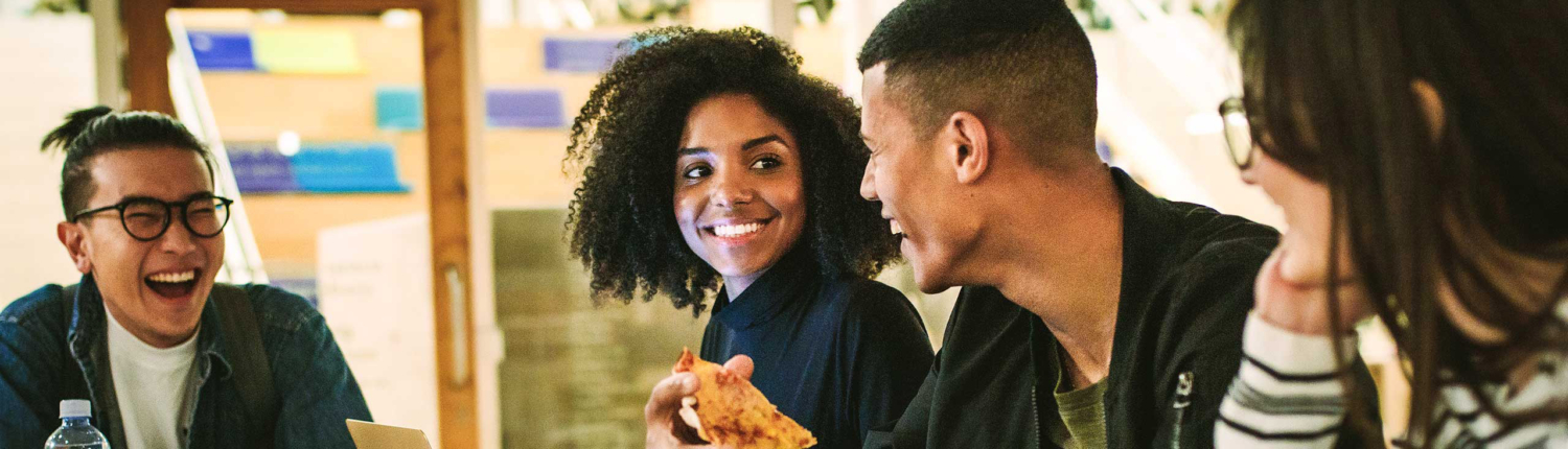 Photo of a diverse group of 4 college students laughing and enjoying pizza.