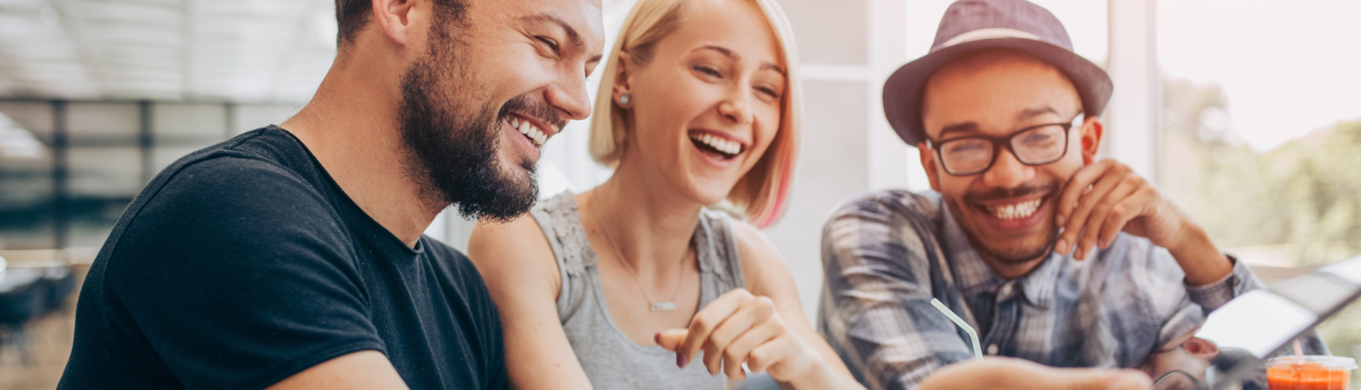 Photo of a diverse group of 4 college students laughing and enjoying salad and croissants while they watch a video.